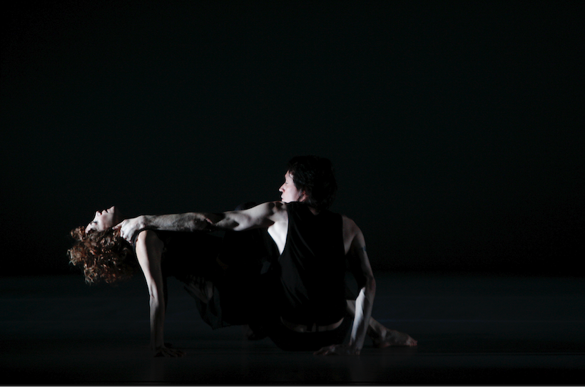 woman leaning back head cradled by man in black very dark image