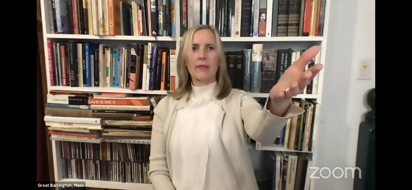 A woman in white gestures in front of a bookcase