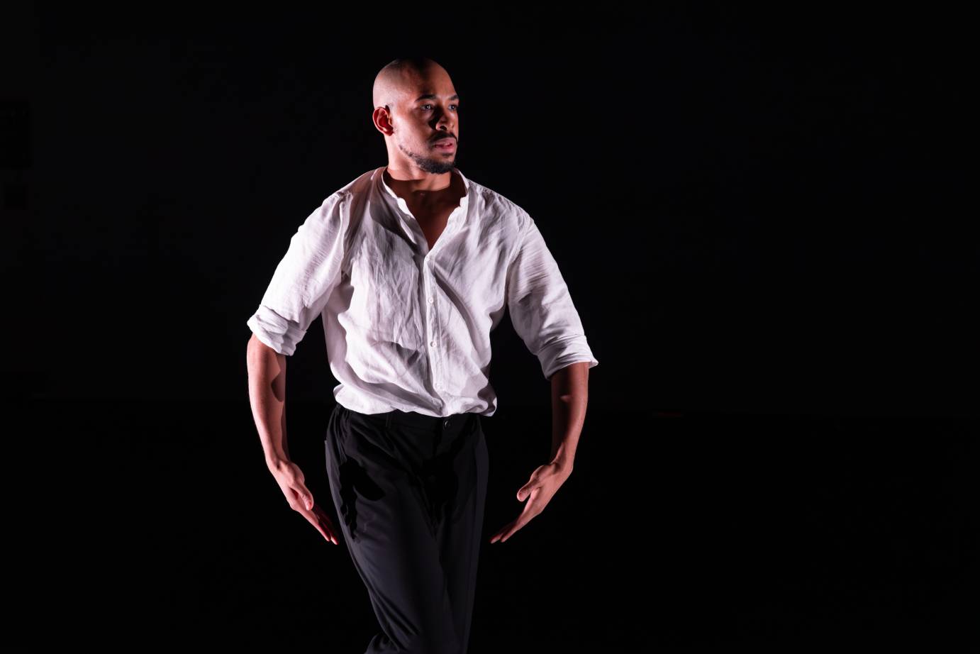 A man in a white button down shirt gazes out on the diagonal. His arms are curved near his sides.