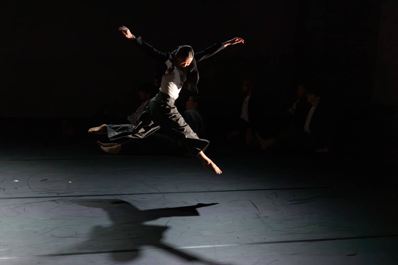 A woman in full leap looks downward as her arms are tossed up.