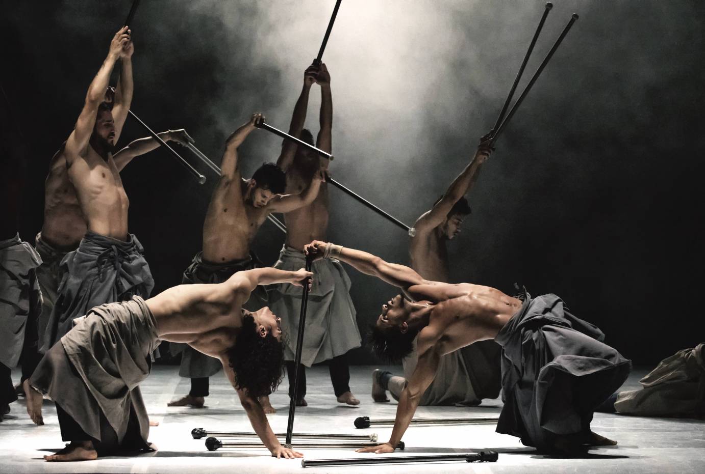 Two men backbend holding one pole as men lifts poles behind them