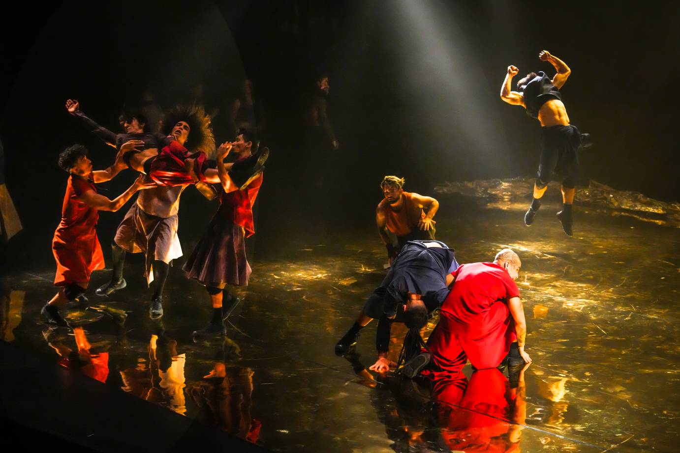 We see three areas of interest on the stage a group to the far right holds a dancer aloft, it seems as if the dancer has just bolted int ther arms. A center group crouches in a huddle. Finally a man in the background jumps into the air as if trying to kiss the air with his bell button.