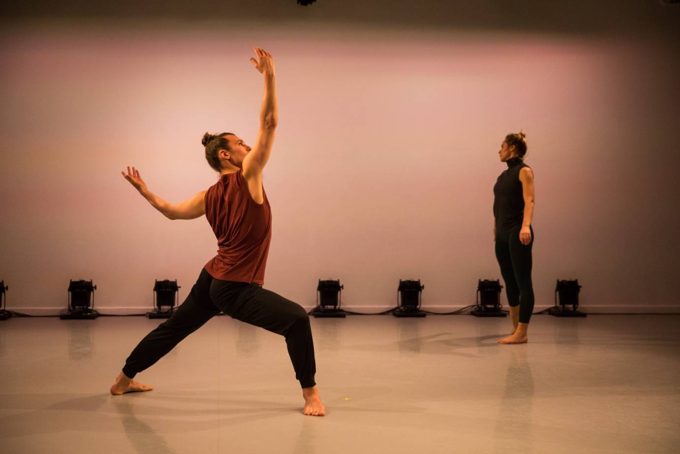 Michael Ingle stands in a wide lunge. His arms are softly outstretched. Alexandra Albrecht is in the background looking away.