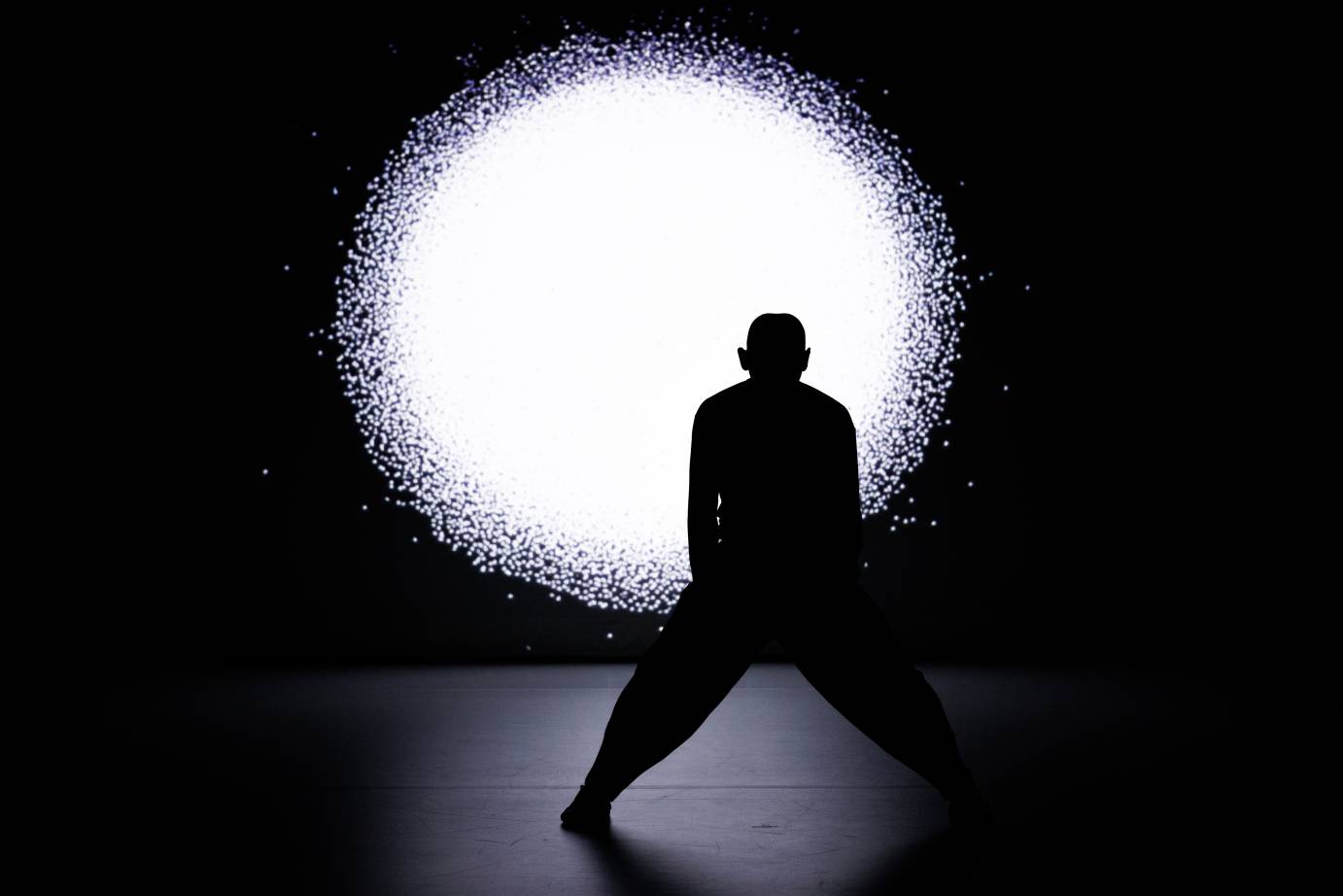 A dancer in silhouette against a sun-like disc projected behind.