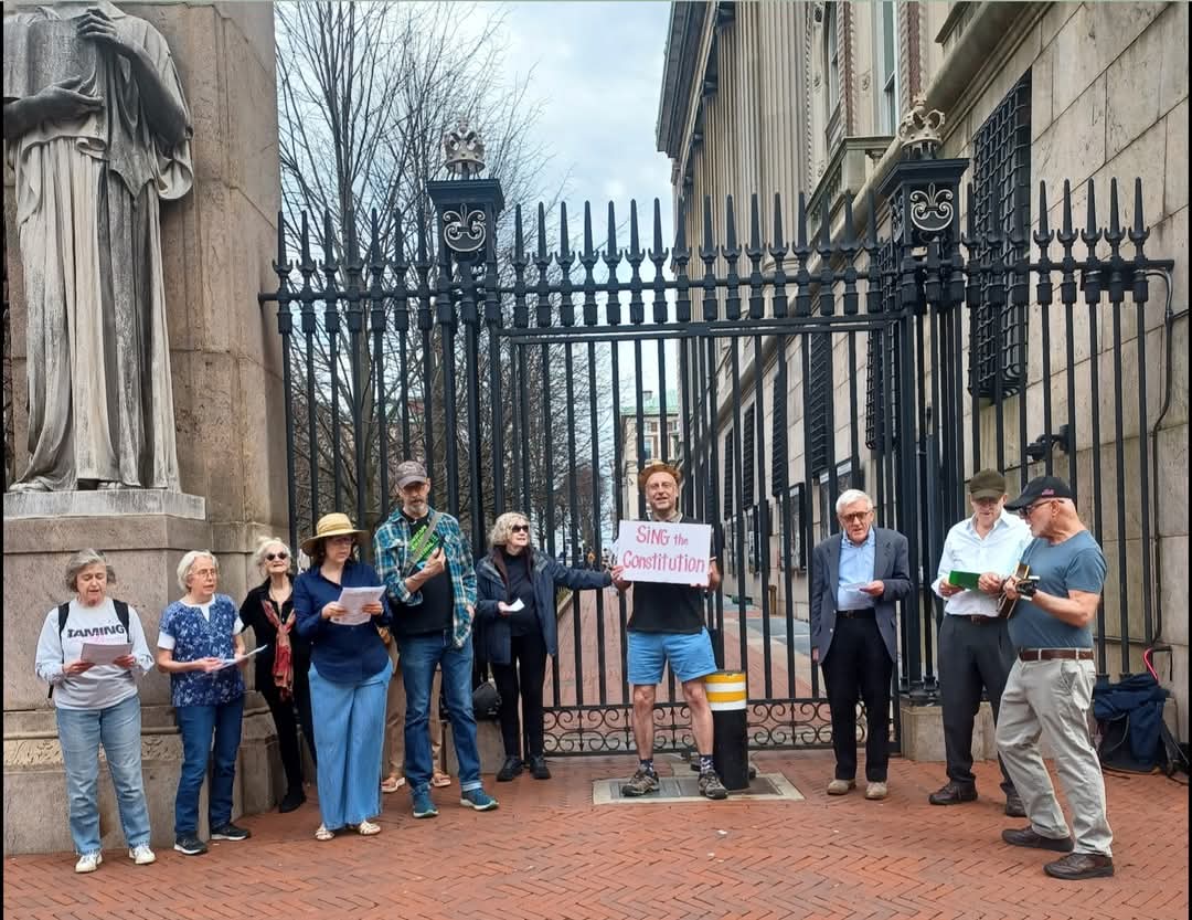 At the wrought iron gates of Columbia University, mostly older people are gathered in protest.