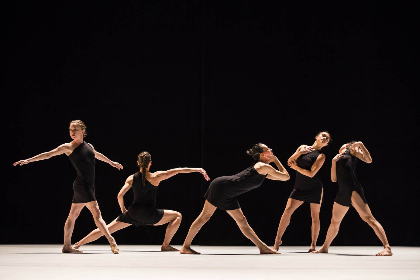 Five women in black dresses pose like fashion models in a line