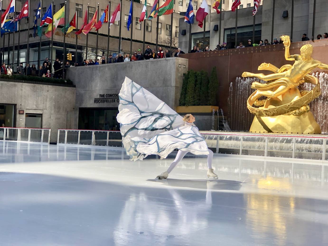 A woman in a white and winged costume gracefully extends her arms as she skates