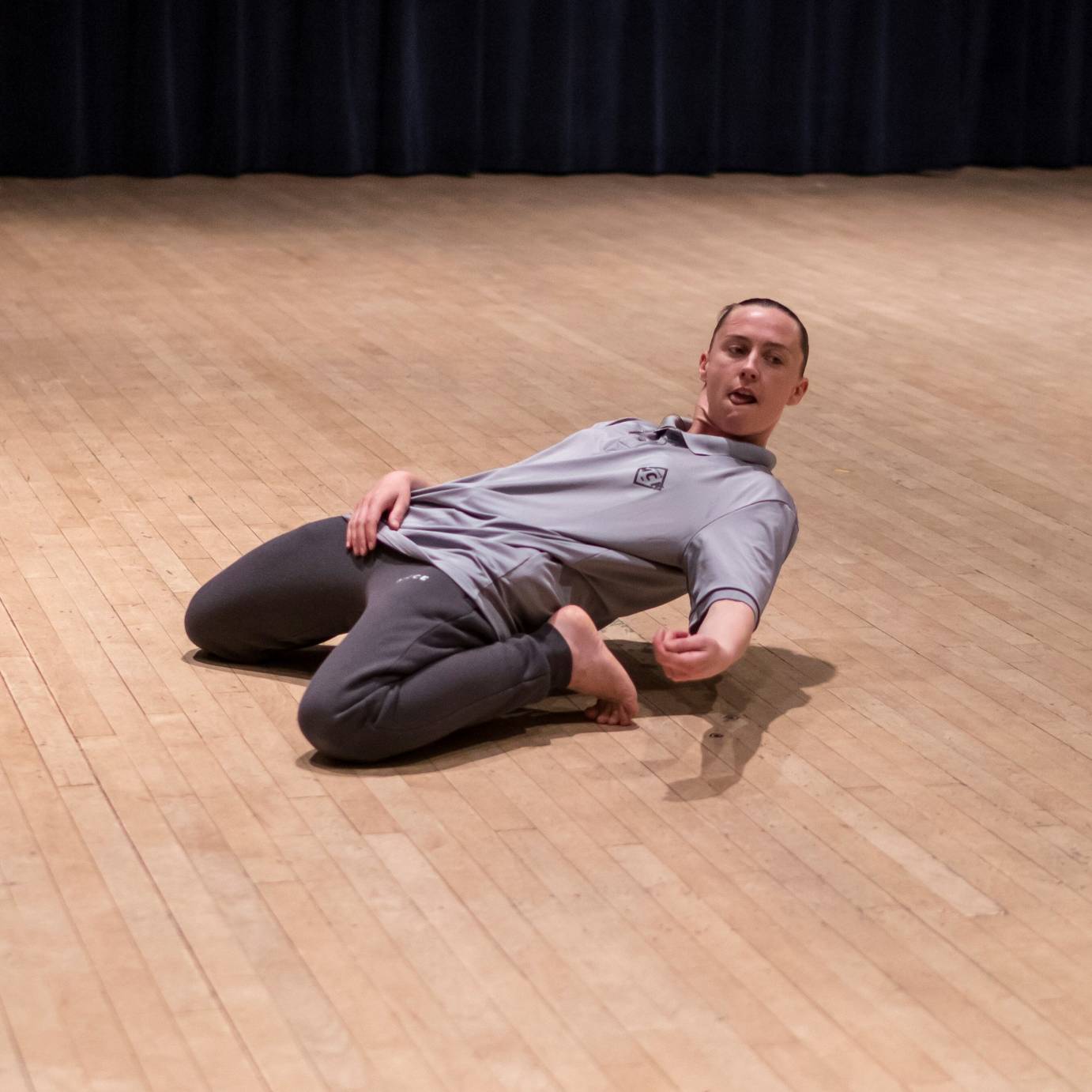 A dancer in sweats and a polo affects a deep backbend while on her knees