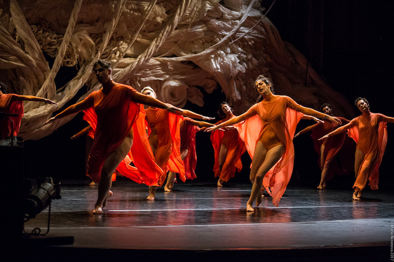 A group of women in orange costumes balance with their arms outstretched