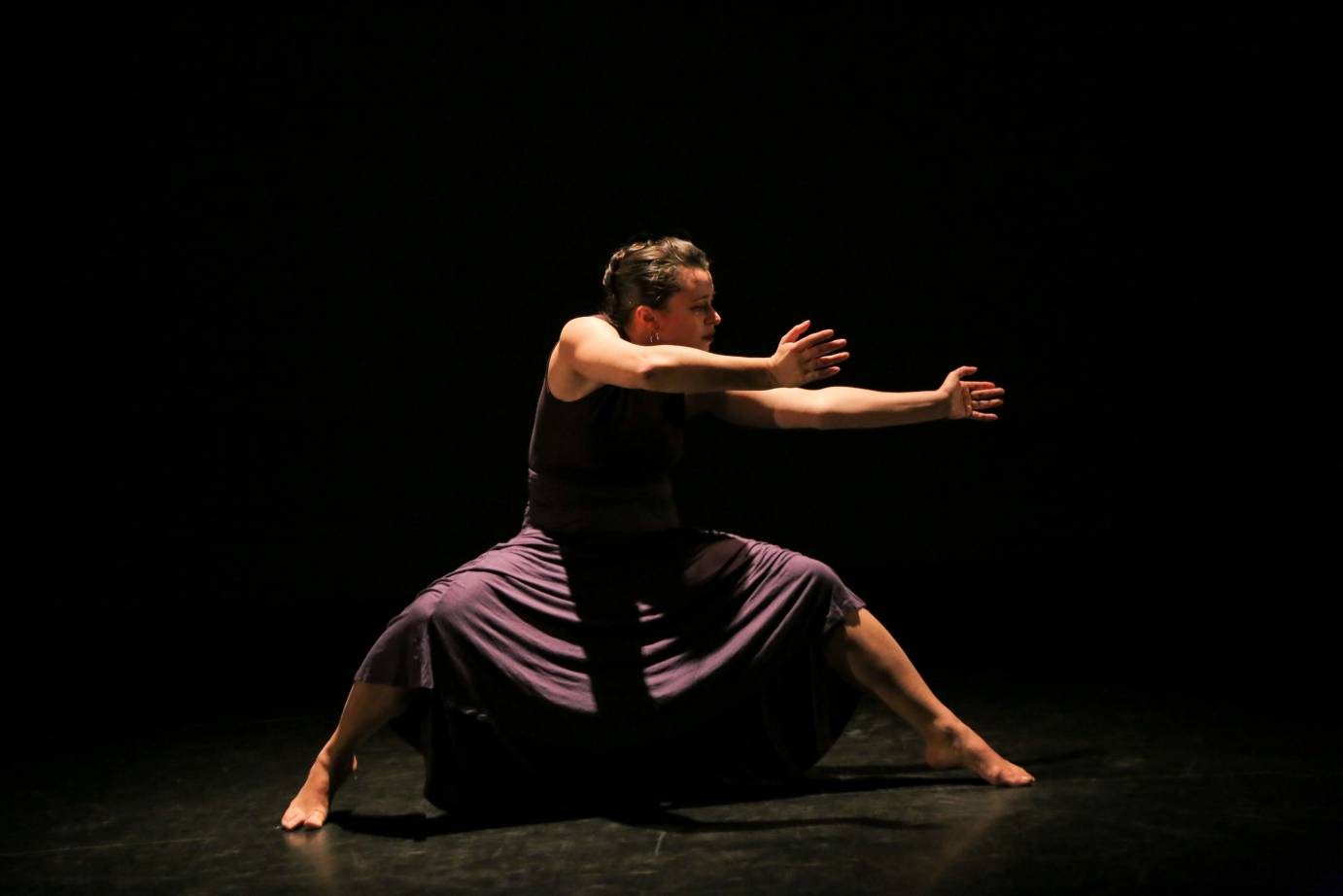 A woman, her legs in a deep squat, stretches her arms to her left side