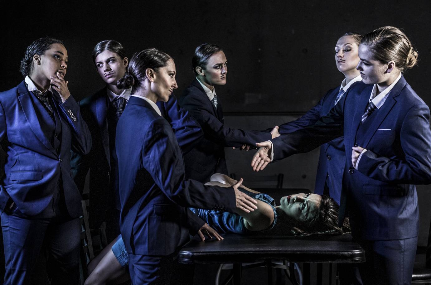 A woman lies down and is surrounded by drag kings