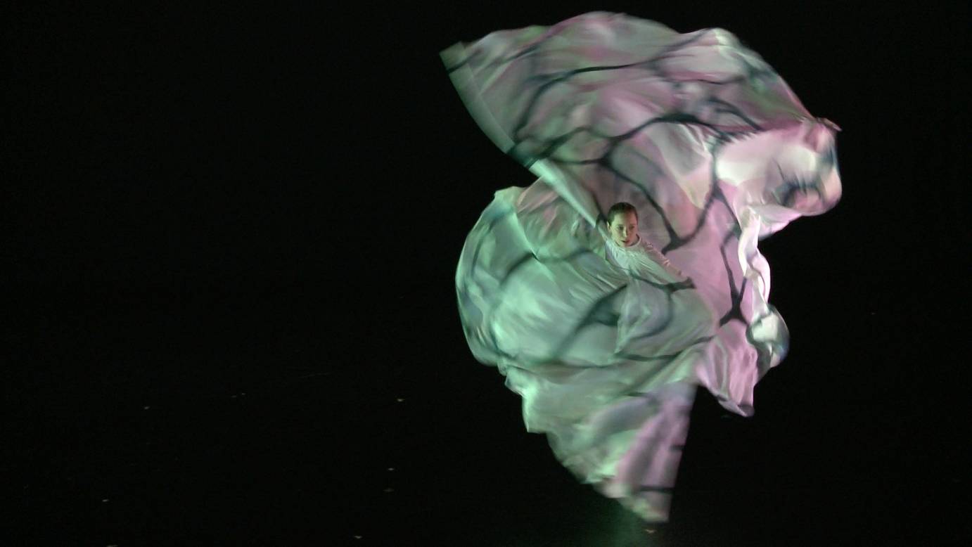 A woman in a flowy gauzy dress spins. The layers of fabric cascade around her.