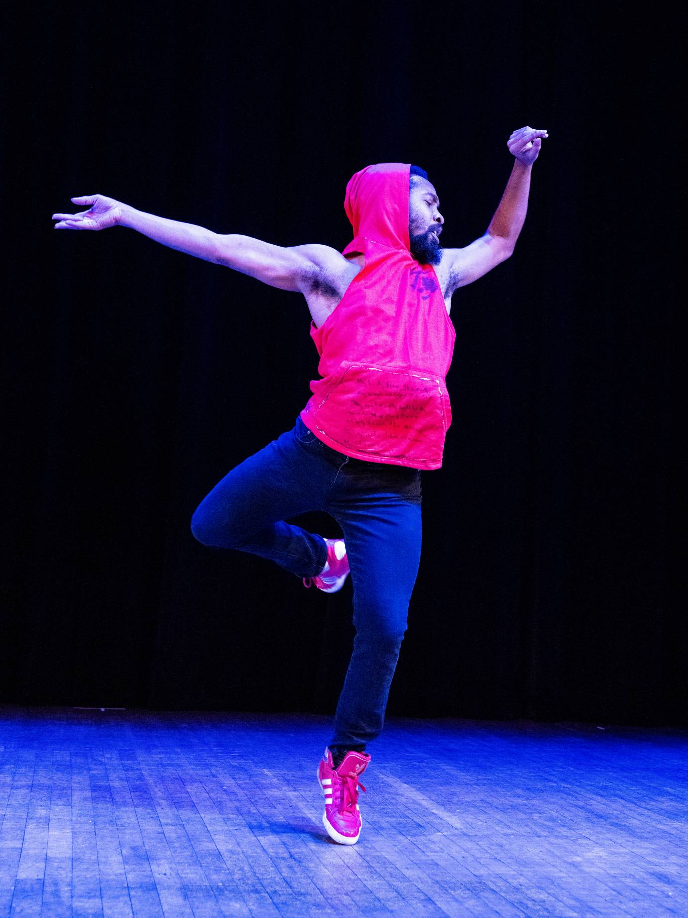 artist Johnnie Cruise Mercer in a translike dance. He wears a sleevless red hoodie, jeans and red sneaker