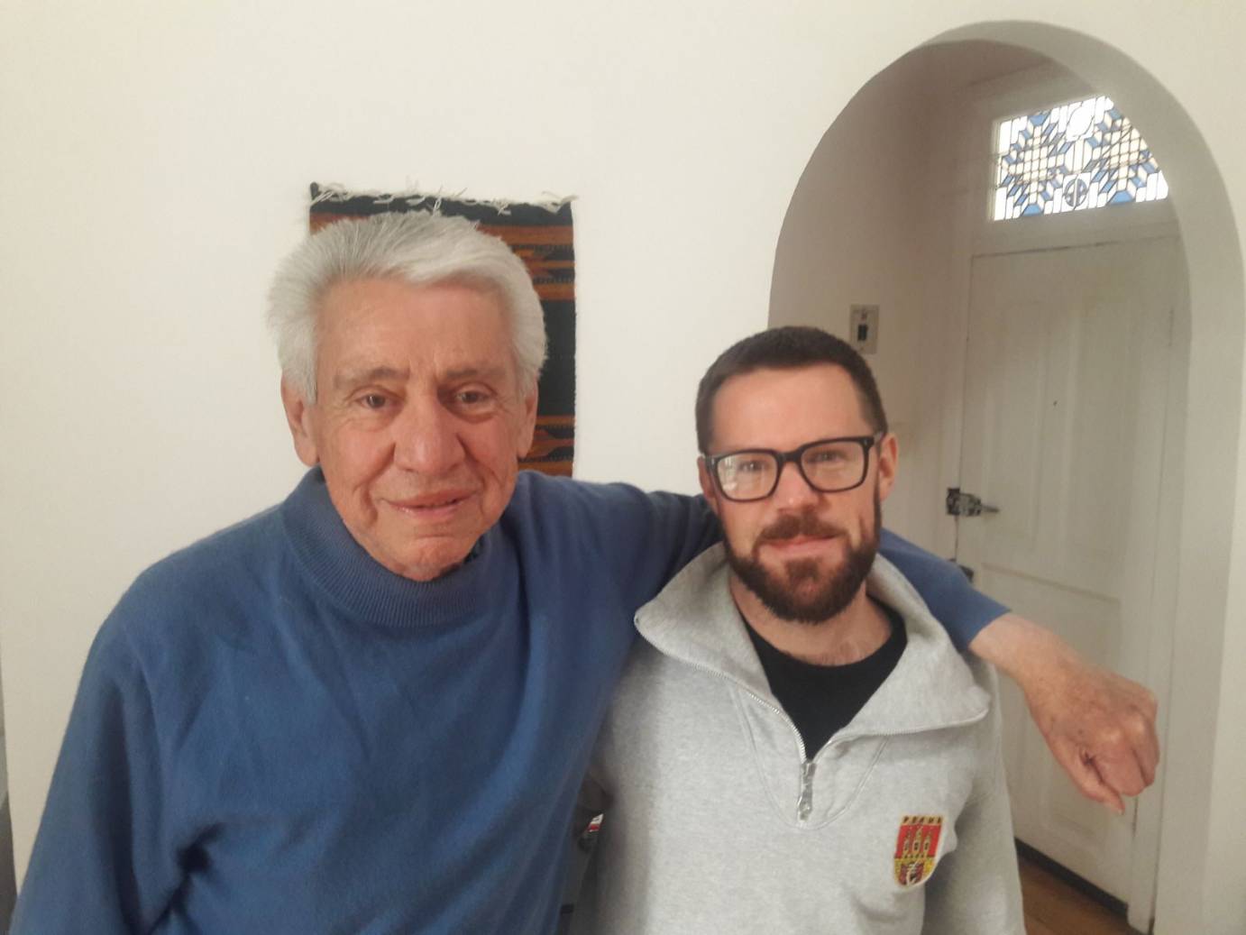 An older man stands with a  young man with glasses