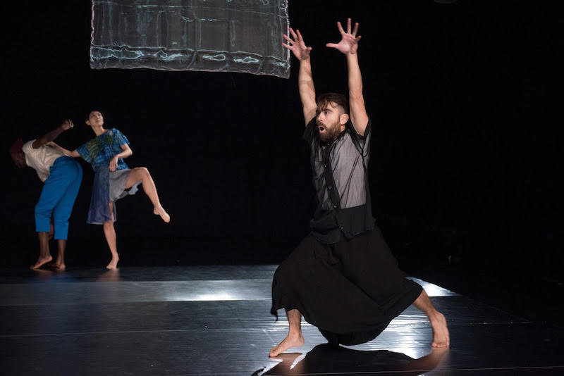 Julian Barnett in a black dress splays his hands above his head