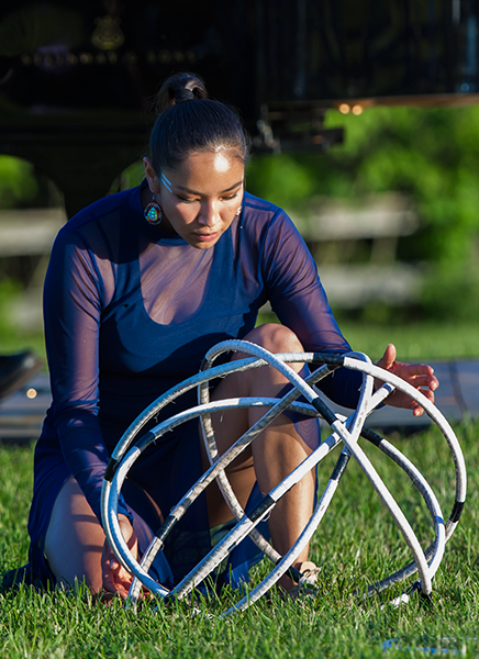 ShanDien LaRance, concluding her dance kneels on one knee, looking down at her hoops, which are melded into a ball in front of her. This prayer like gesture acknowledges Mother Earth.