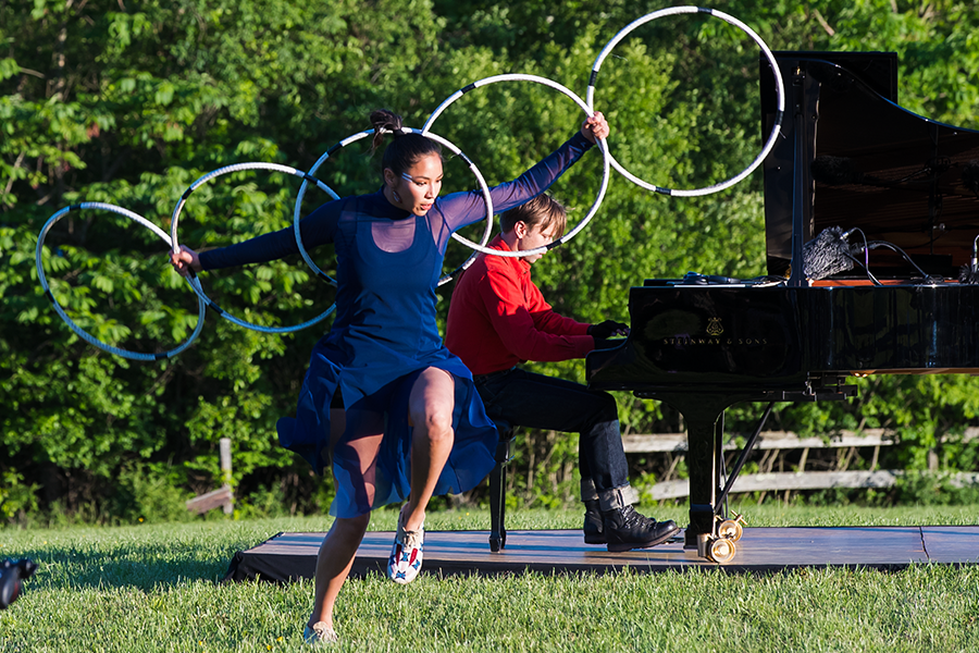 ShanDien LaRance, native American dancer, wearing a royal blue dress, with a short skirt and sheer sleeves, dances on the grass in front of the grand Steinway. She again emulates a birds wings with her hoops. 