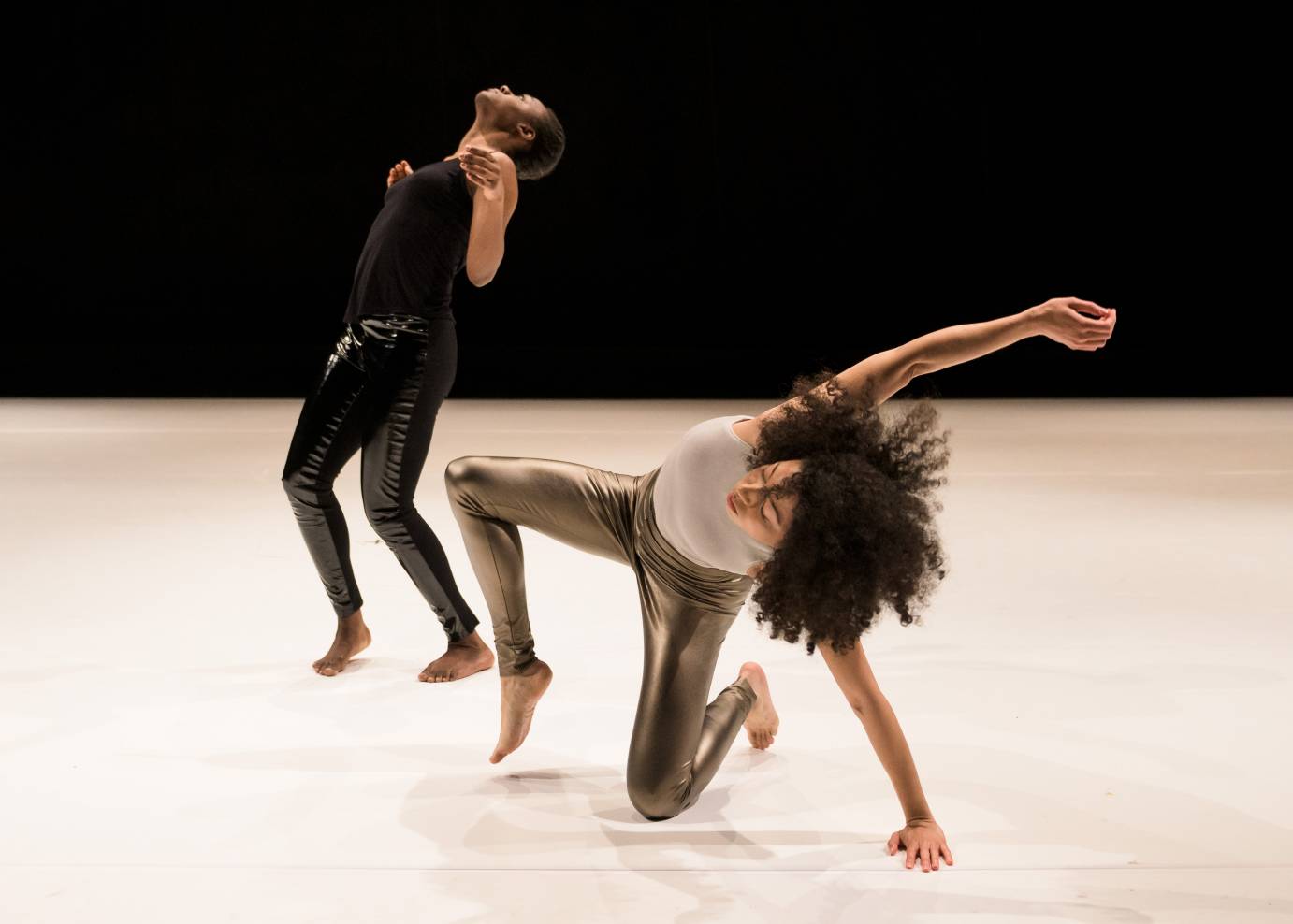 Two women arch their backs, one standing, the other  kneeling