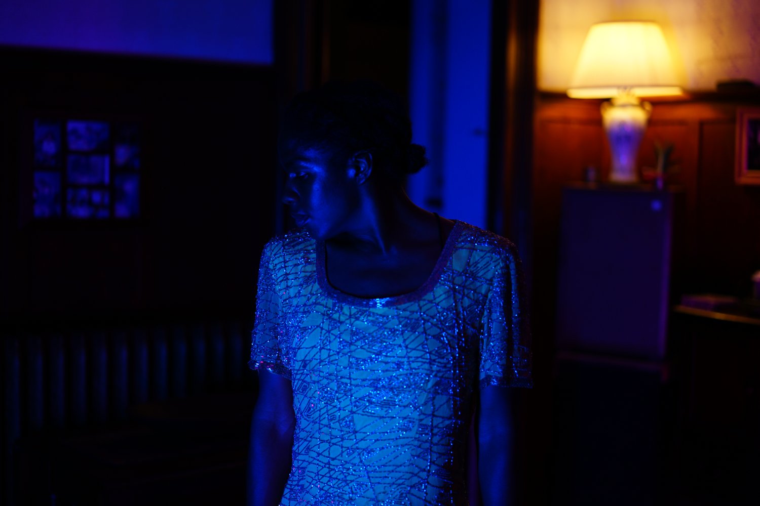 Kayla Farrish in Film shot, a darkened room in profile, wearing a yellow and blue dress covered in glittery beads 