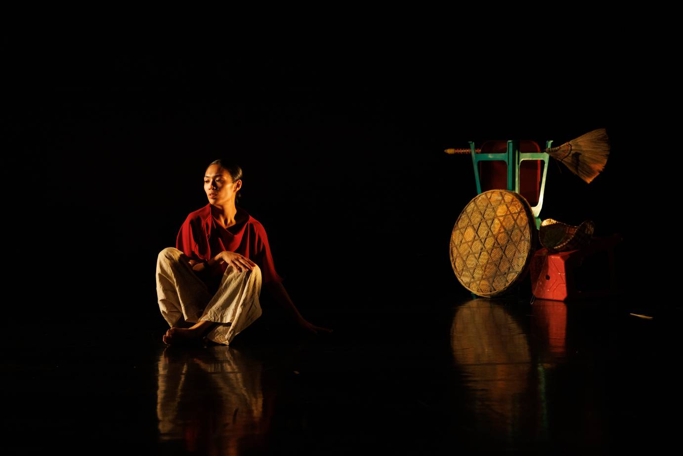 A red-shirted woman sits contemplatively infront of a round tray and stacked kitchen apparatus.
