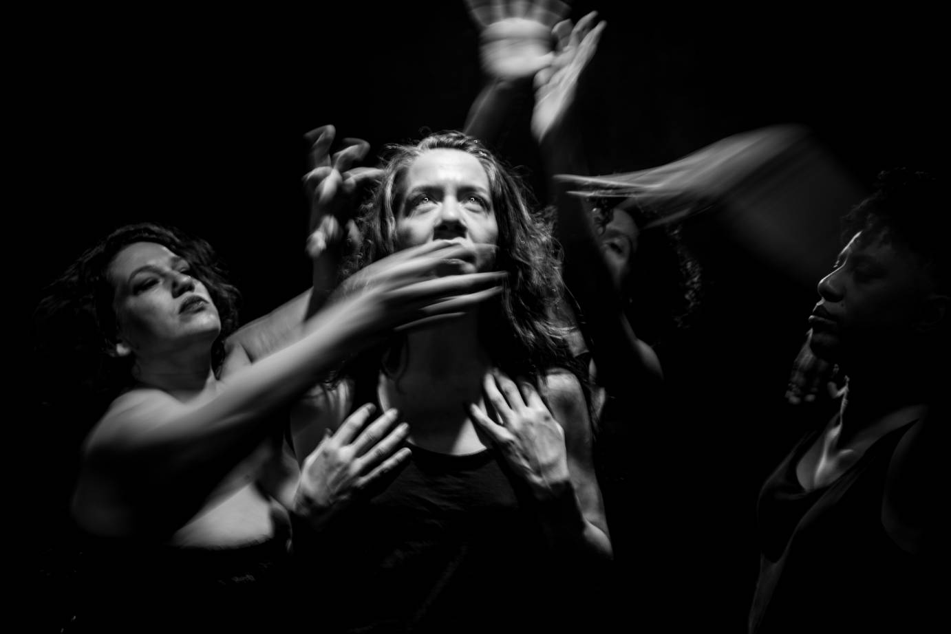 One woman has another woman's hand over her mouth while two others wave their arms