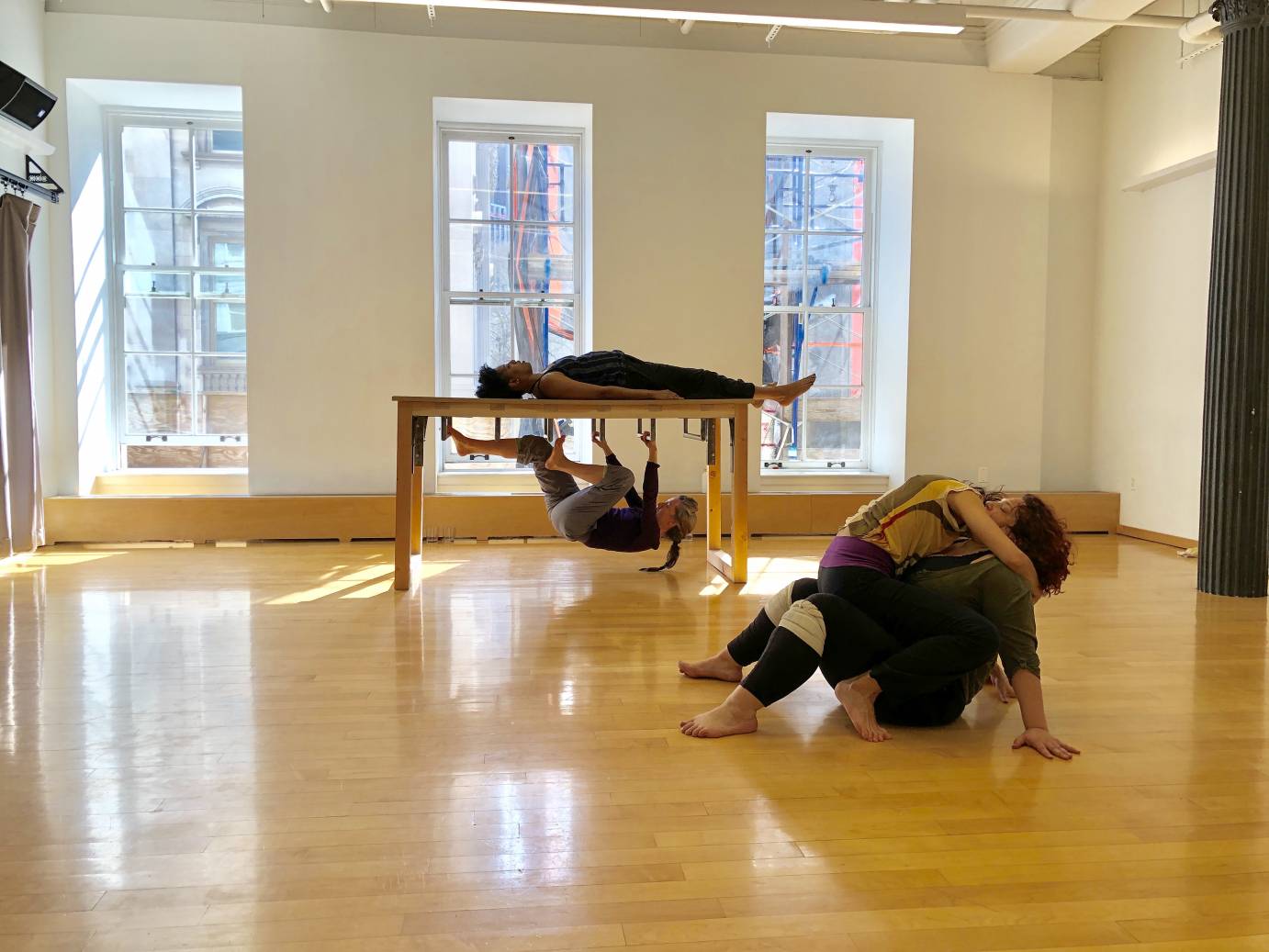 Two women cuddle downstage while one woman lies on a table as another plays underneath