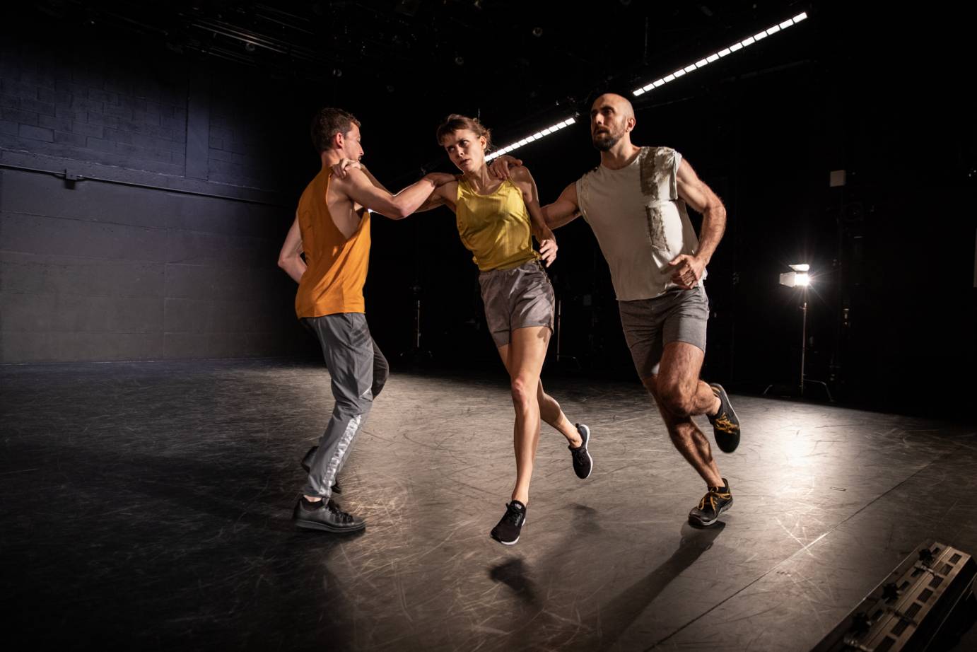 Three dancers run, holding on to each other's shoulder