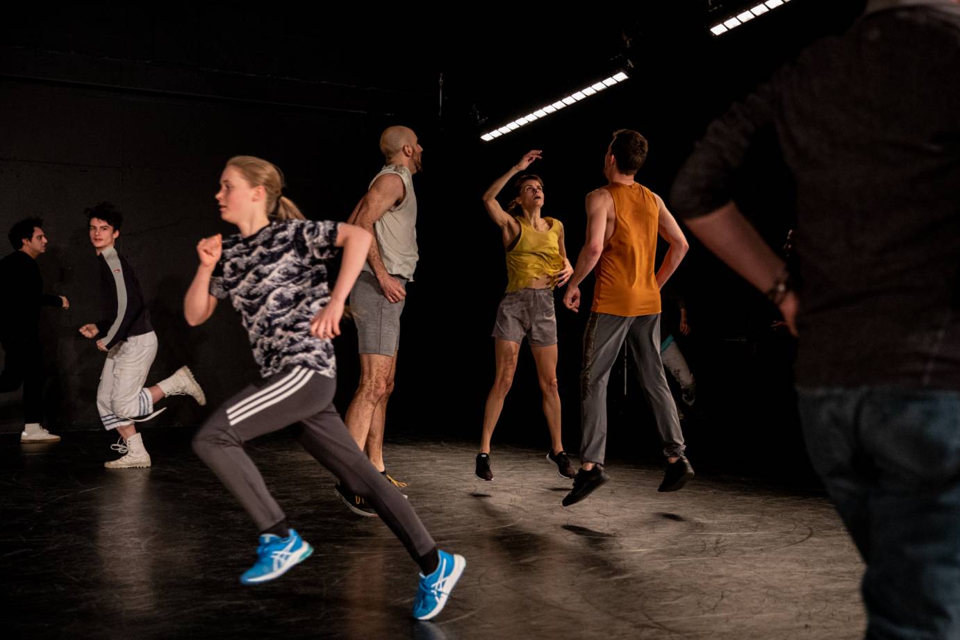 Three dancers jump stage center as people run around them