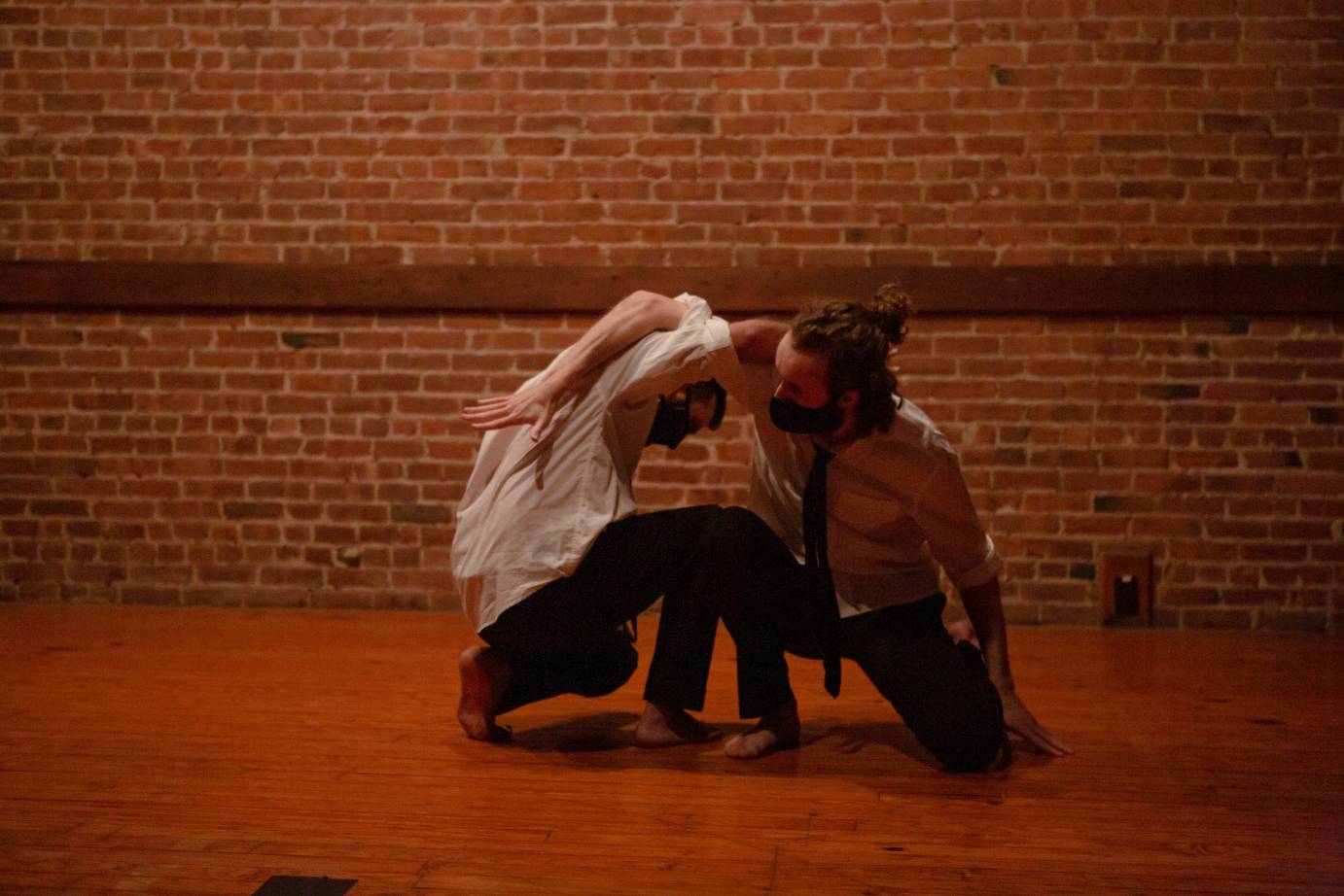 Two kneeling men in white dress shirts and ties hook arms around each other