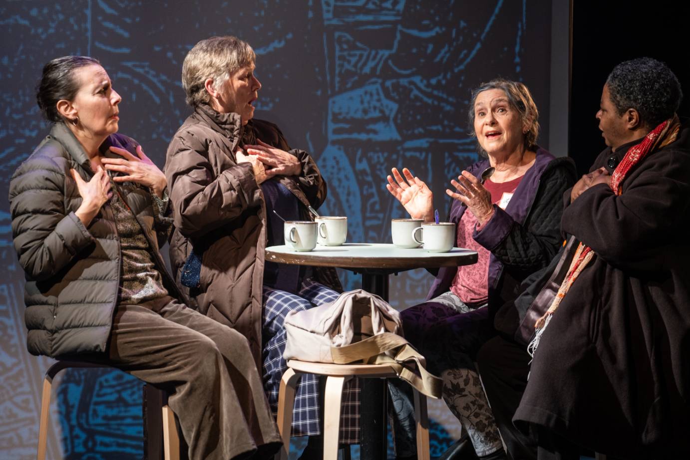 Four older women in winter coats talk while sharing coffee 