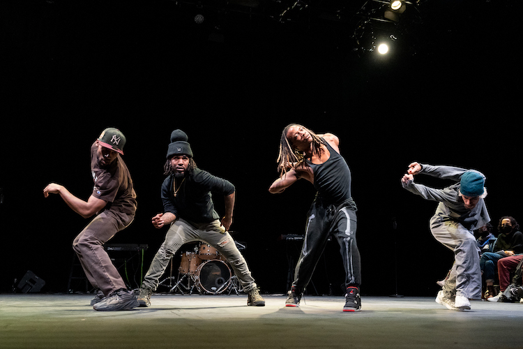 a group of 4 Black male Flexn dancers create at tableau of shapes. They all wear casual streretwear in dark colors. Everyman has a cap on except for one who sports long light tinged dread locks