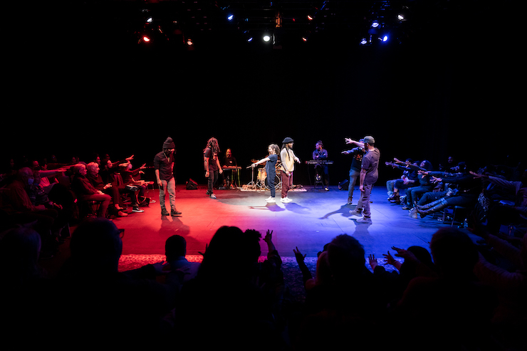 the audience and artists form a circle and lift their arms upward... a cypher, immersion
