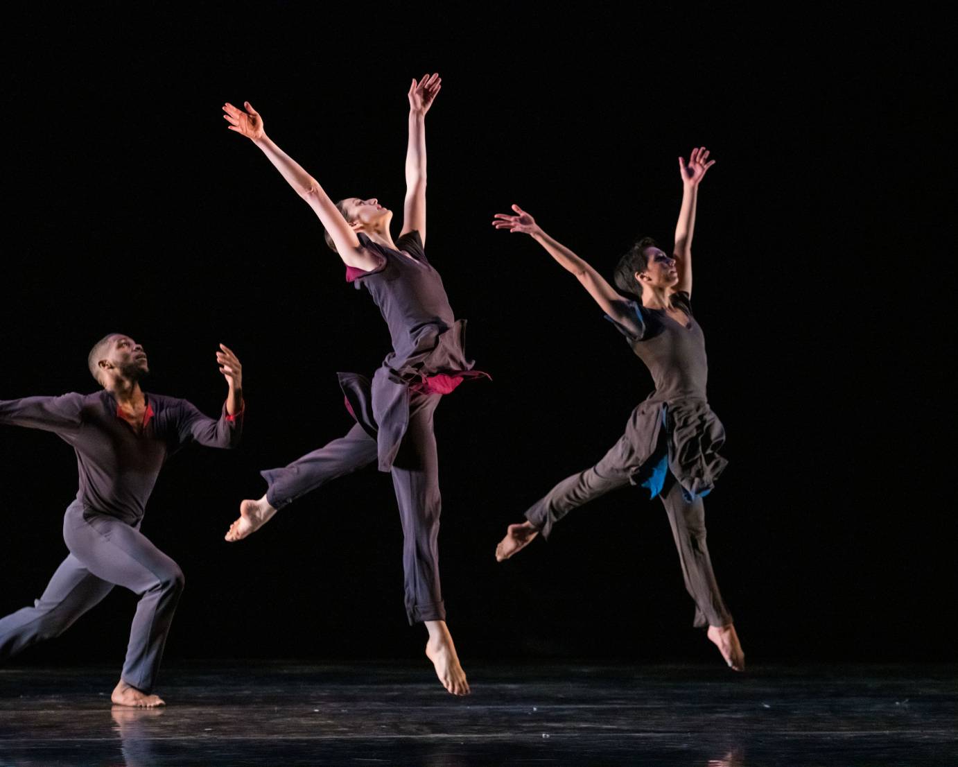 Two dancers leap to heaven, their arms extended, as one man runs behind them