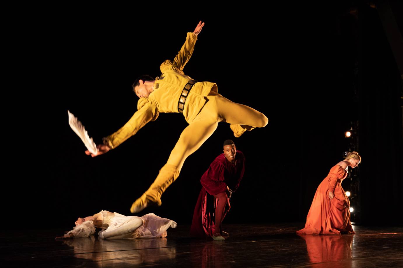 A man with a knife leaps in the air as two women and one man hunch in the background