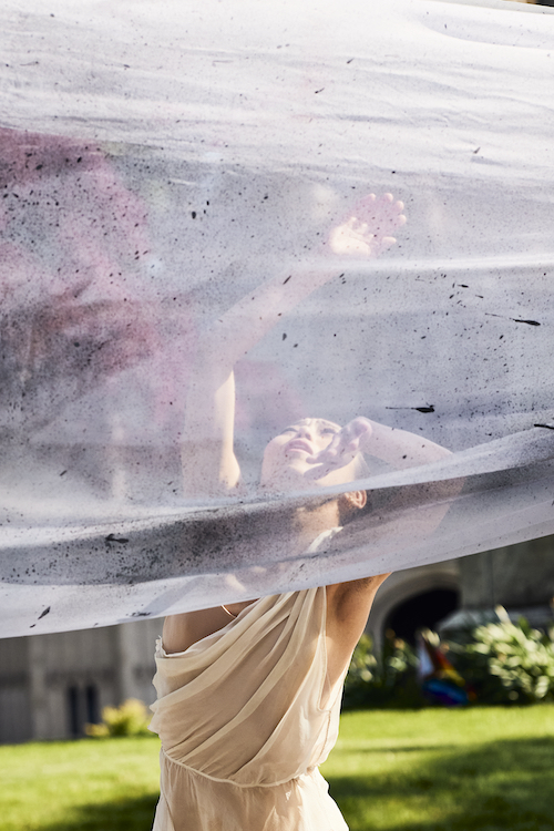 a dancer reaches upward towards a wave of sheer gauze that envelopes her torso