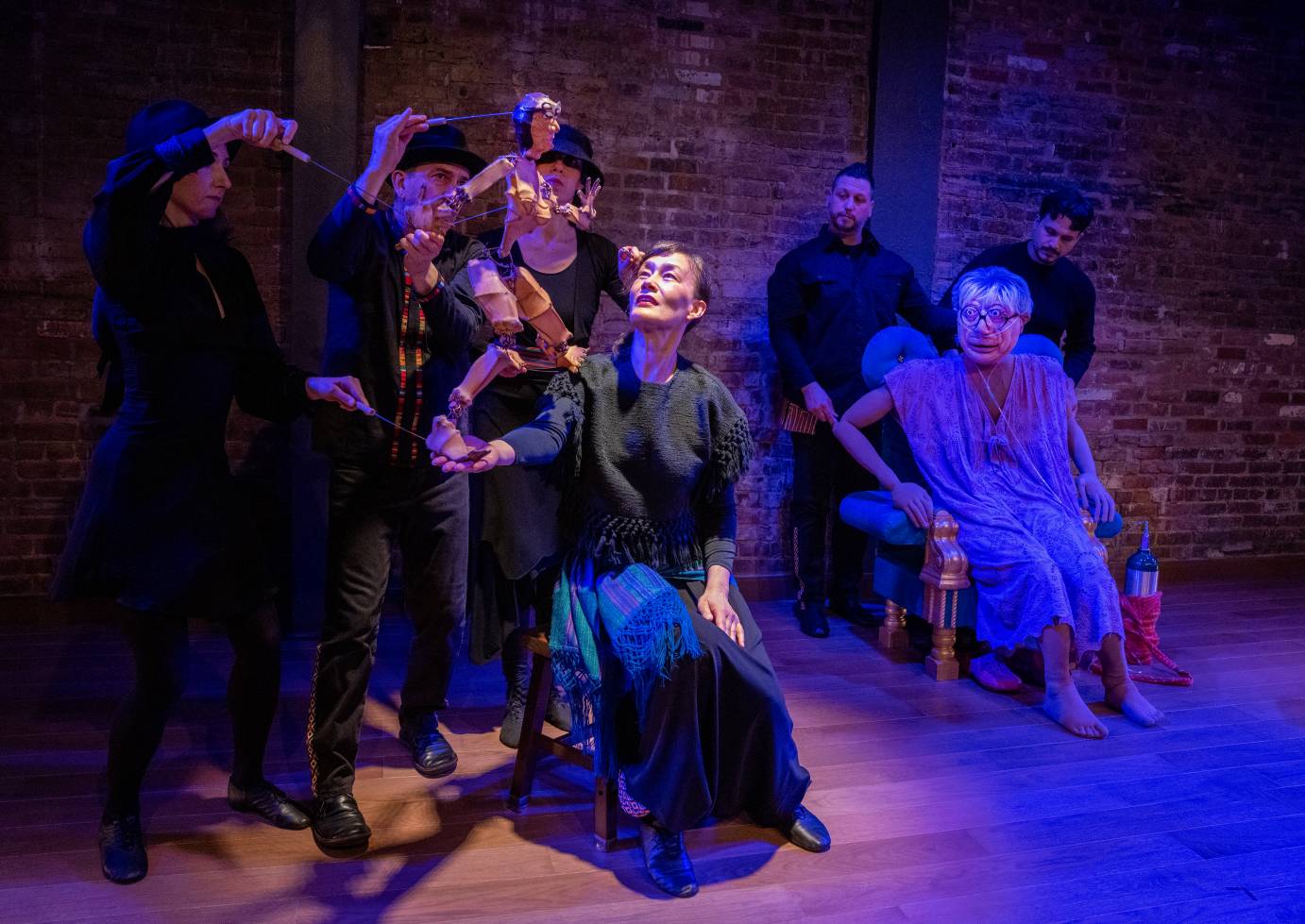 Three puppet handlers work with a flesh-colored 2' high Sonia puppet representing Sonia as a young woman. The older puppet Sonia sits in her padded chair with her two puppet handlers looking on