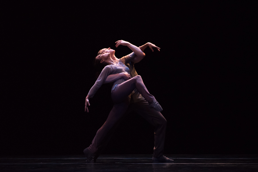 A man embraces a woman. Her front leg comes off the ground. They look towards the heavens.