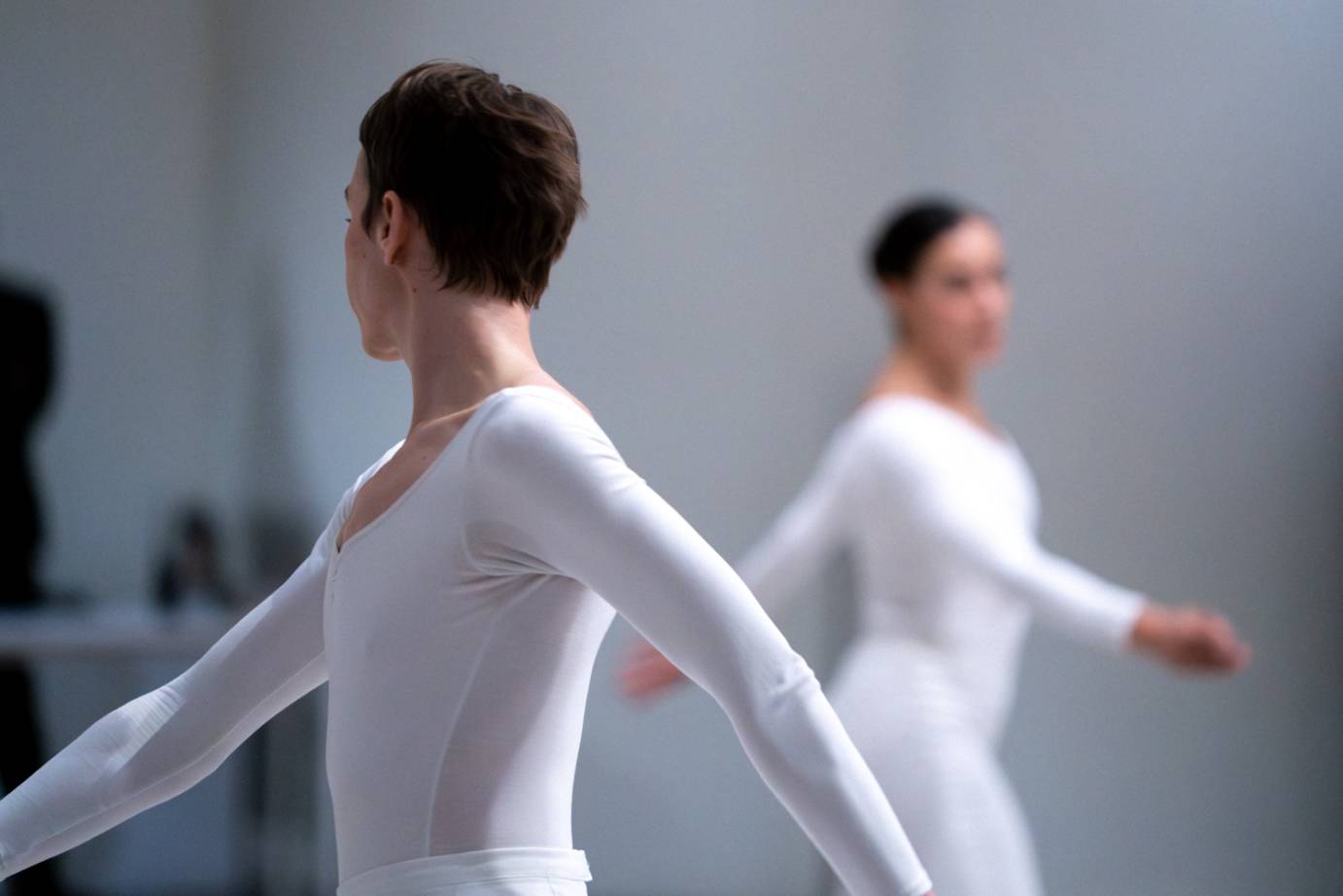 Two women costumed in white turn their heads toward each other as they pass by. 