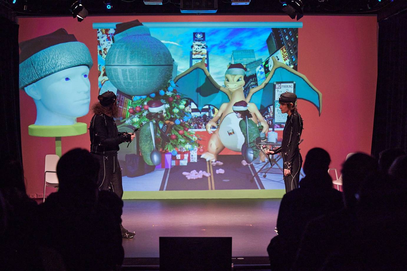 Two dancers in black stand in front of a colorful collage projection