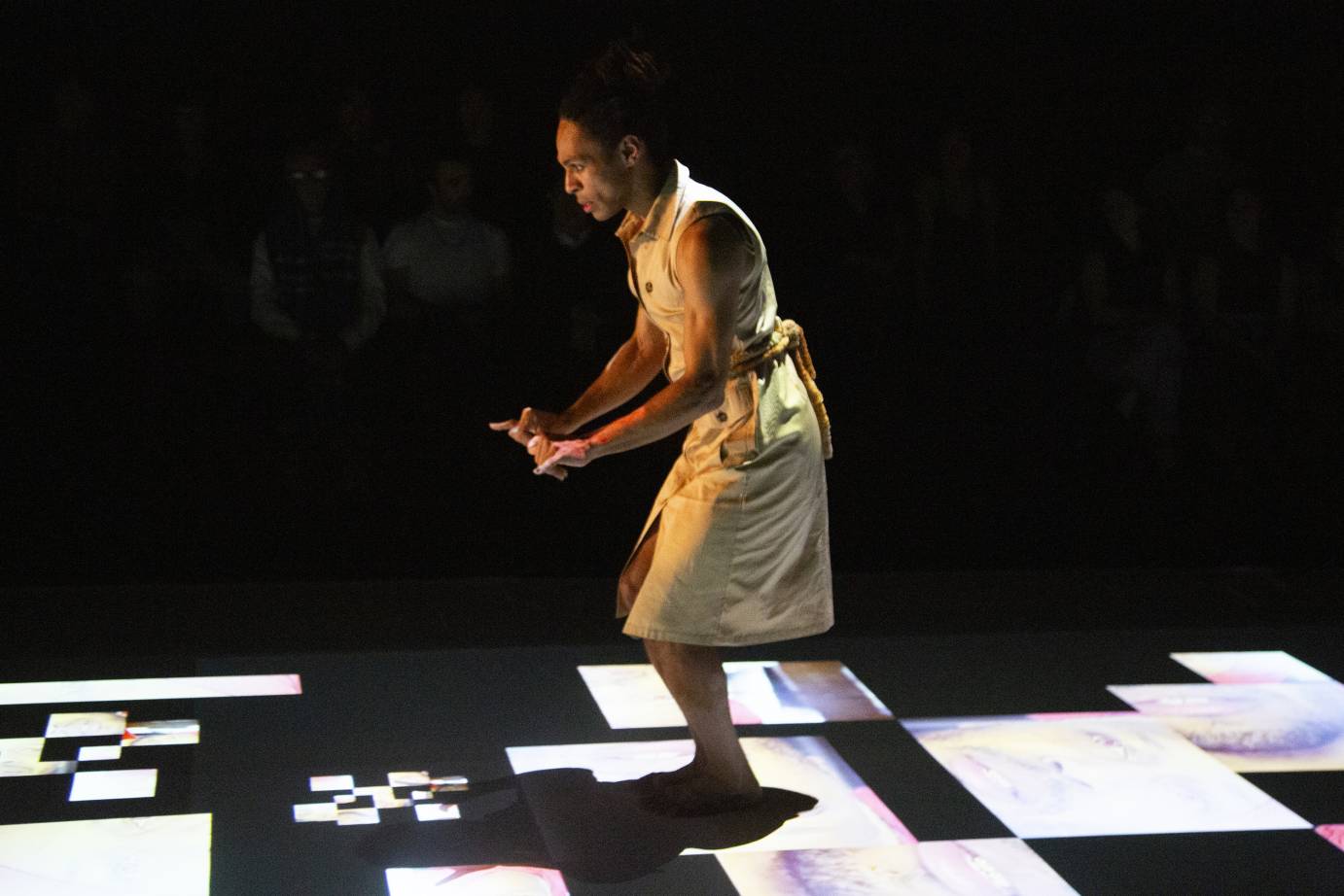 A man dressed in a yellow shift prances on the film projected onto the floor.
