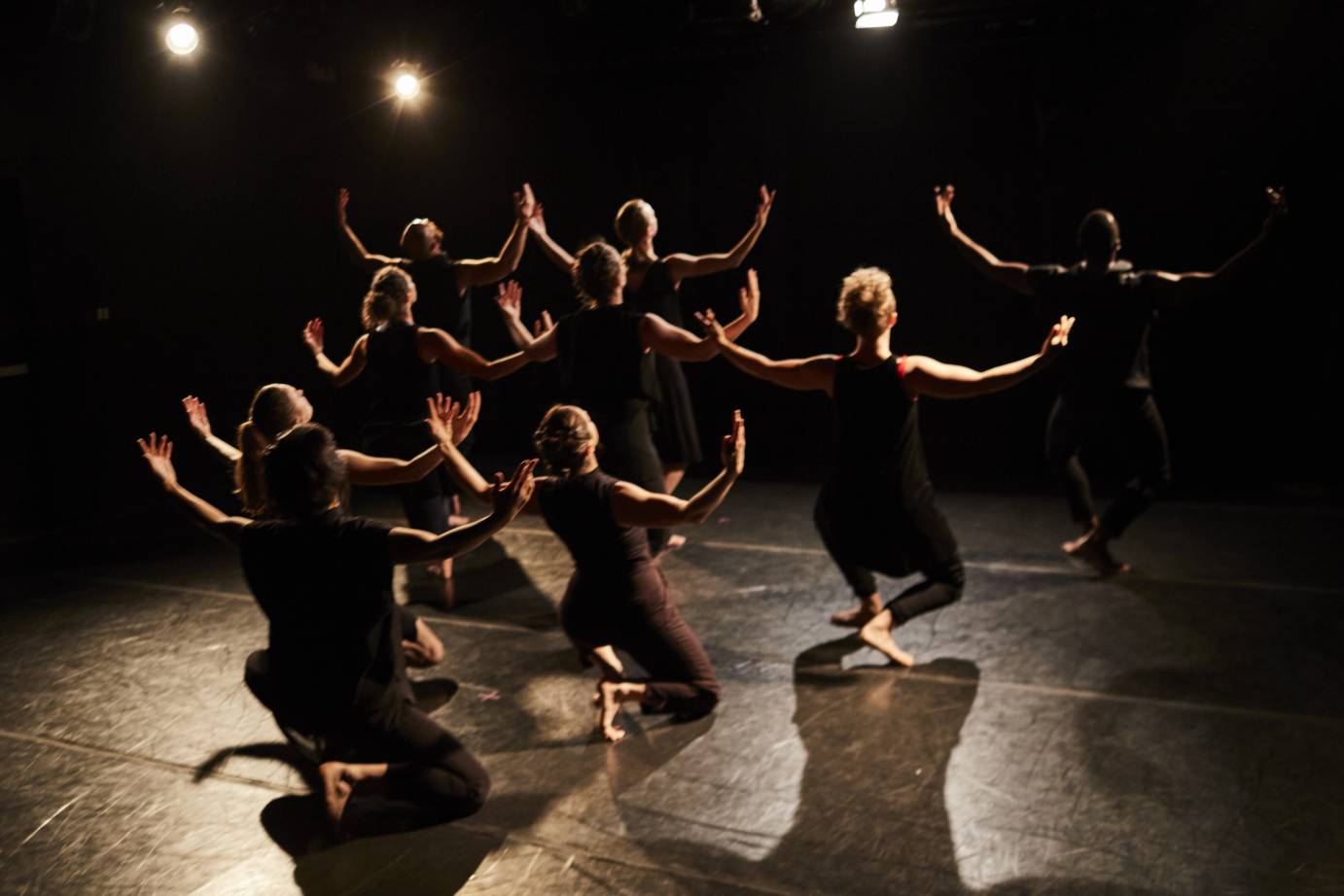 Dancers form a cascading pyramid, front to back, arms lifted to the side