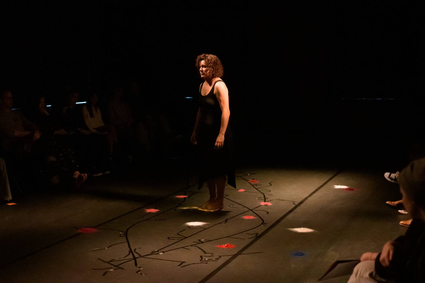 Woman in black dress stands with clumps bright powder around her