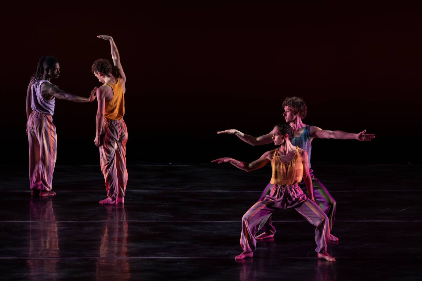 Two couples - one stage left, looks to their right with their right arms lifted chest-high wrists limp while standing in a tight second position. The second couple stands in close proximity to one another and situated slightly upstage. One man's arm is lifted while the other places his hand on the dancer's chest.