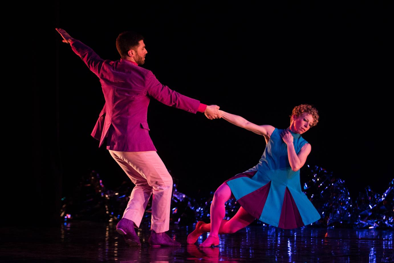 A woman and a man lean away from each other while holding hands