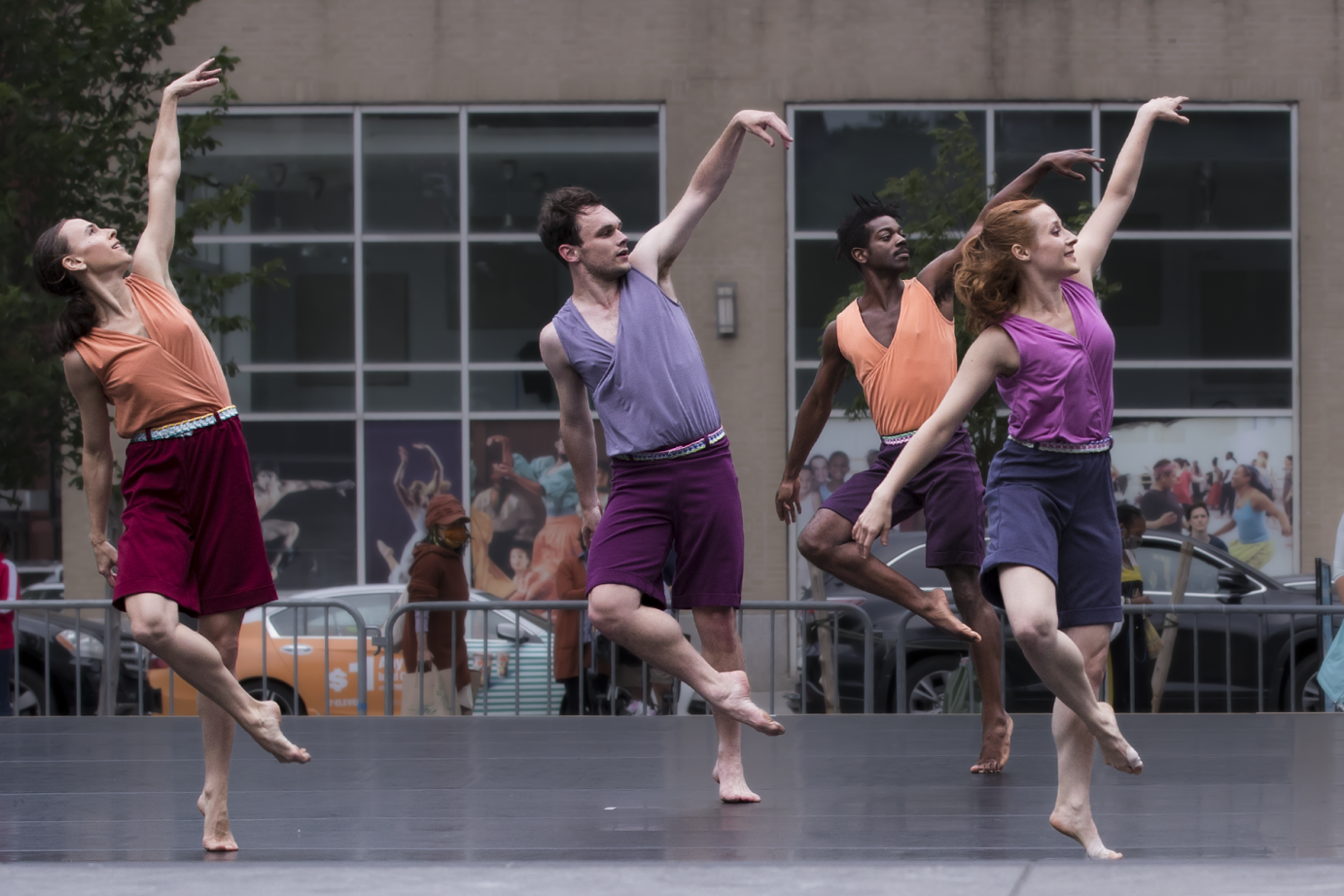 Four dancers in the midst of movement. Their bodies are leaning to the right.the