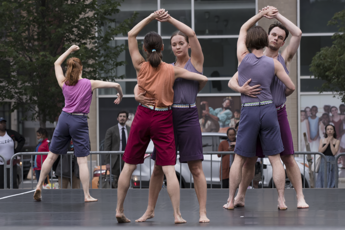 two couples a woman and woman and woman and man hold hands as if dancing together. to their side one lone woman seems to dance with an invisible partner