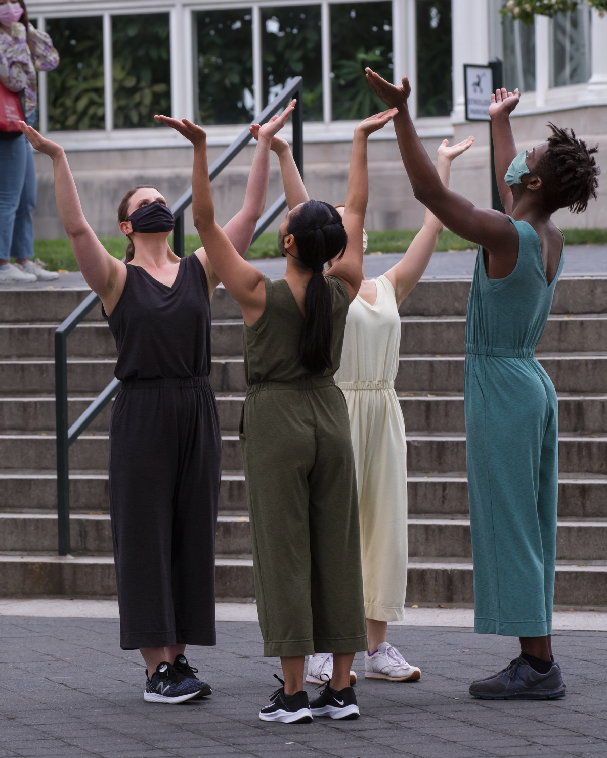 Four dancers performing outside wearing masks..extend their arms and chest to the heavens