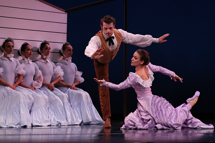 the four followers sit against the white wall of the house set, seated erect with hands clasped identically in prayer, the bride knees on the floor and lift her palm towards the husbandman who leans forward in an arabesque to meet her palm