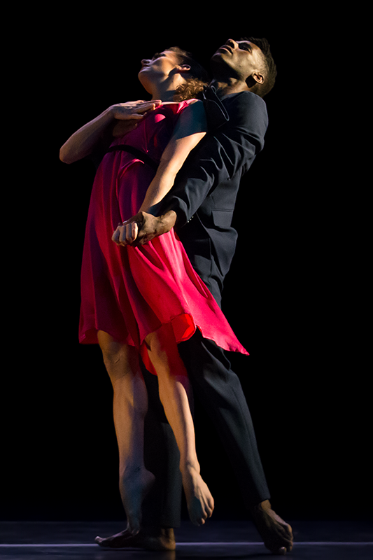 The woman's feet graze the floor as her partner lifts her up leaning her against his chest. They both face frotn but he looks directily upward while she casts her eyes upward on an angle.