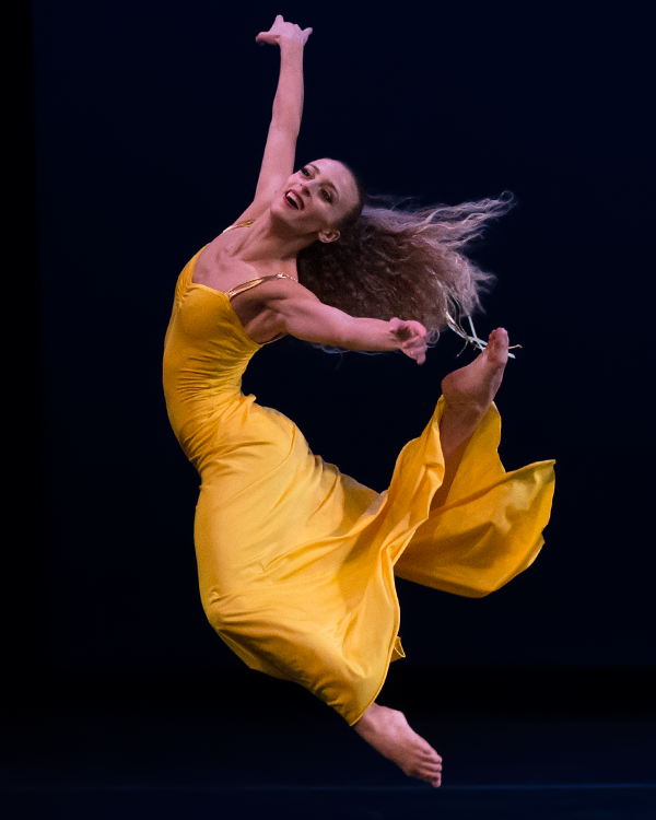 the smiling woman in yellow floats in mid air as the result of a huge jump with a double back kick.